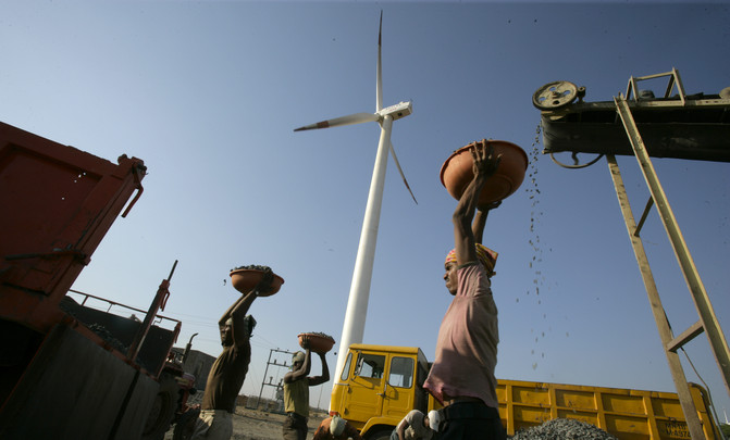 A laborer is seen working at a deisel powered crusher infont of a wind turbine.